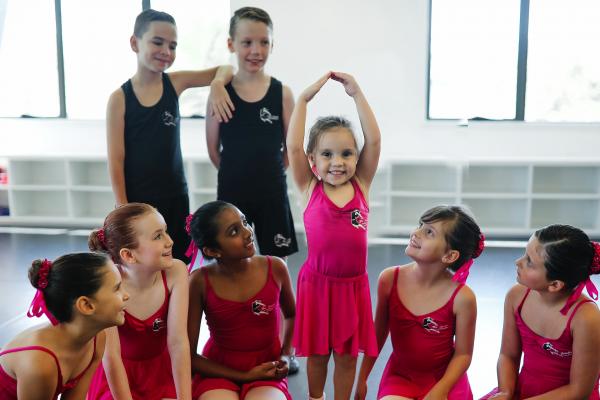 Colour photo showing eight children supporting a younger child who is learning to dance