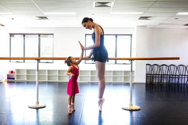 Colour photo showing an older child in pointe shoes an d a younger child reaching for her 